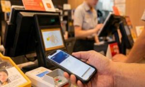 マクドナルドのレジで白い決済端末にスマートフォンをかざしてVisaのタッチ決済を行う様子