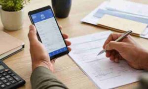 スマホでネット銀行の口座情報を確認しながら書類に記入する手元