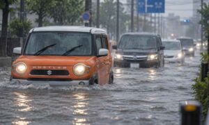 激しい雨で道路が冠水し、複数の車が水につかりながらゆっくり走行している様子